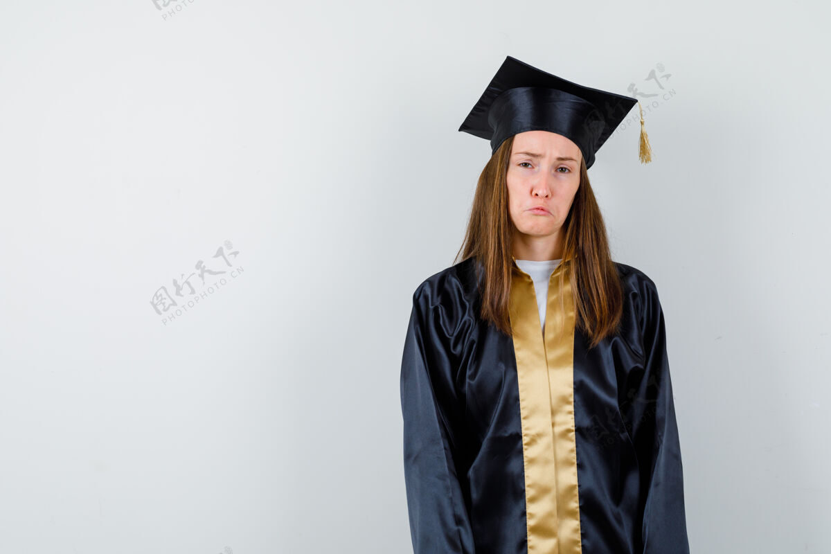 人女毕业生看着相机 弯弯的嘴唇 皱着眉头的脸 穿着学院服 看起来很悲伤前视图欢呼学术多样性