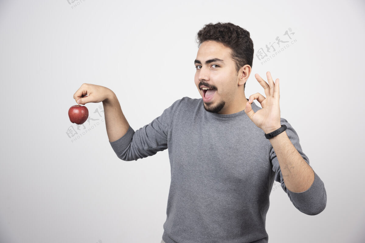 男孩一个黑发男人拿着一个红苹果站在灰色的树上举行模型水果
