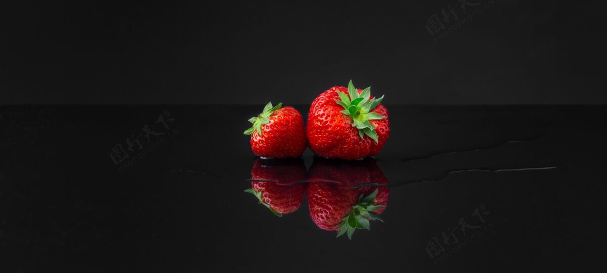 水平在黑色反射面上水平广角拍摄两个红色草莓新鲜角度葡萄干