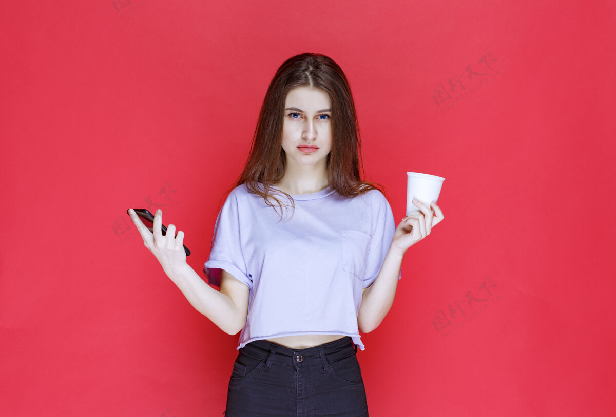 女人一个年轻女子拿着一杯饮料和一部黑色智能手机 脸上露出失望的表情攻击性人悲伤