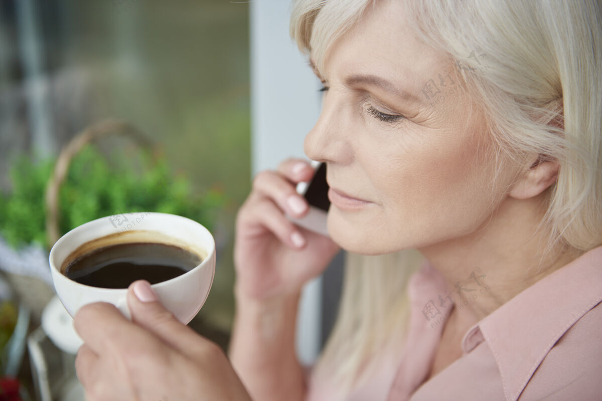 女士在阳台上享受美味咖啡的熟女特写镜头老年妇女手机咖啡