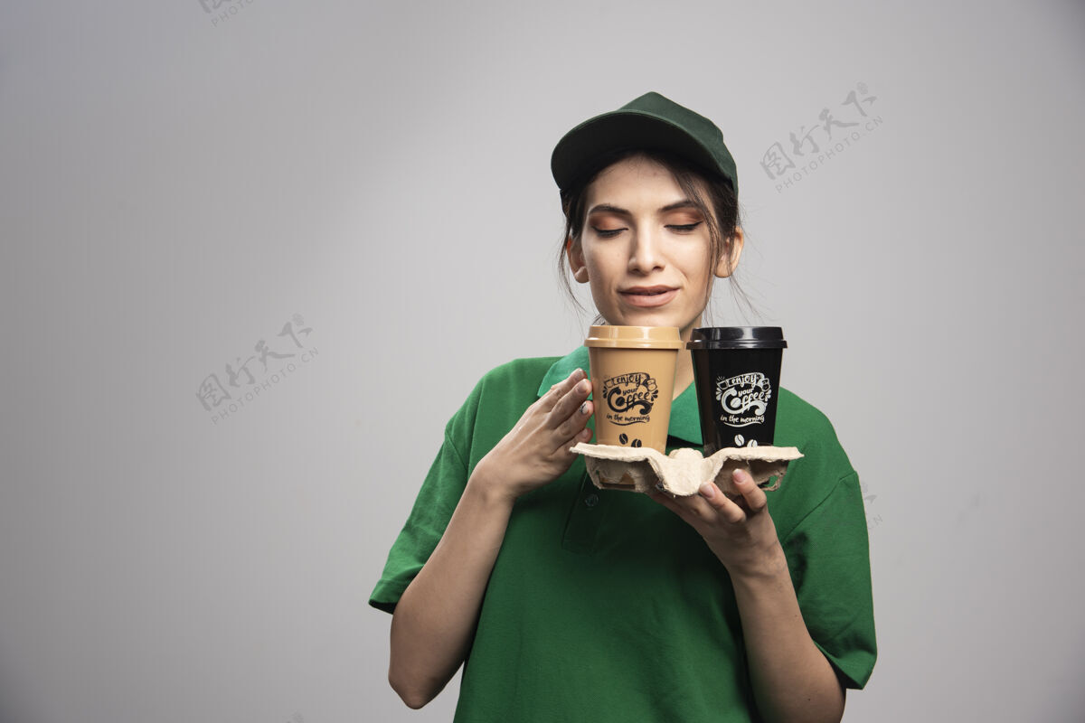 女性穿着绿色制服的女送货员拿着咖啡摆姿势送货制服工人