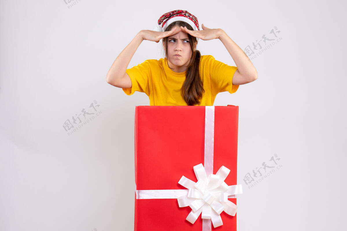 帽子前视图迷惑了戴圣诞帽的女孩把手放在额头上站在圣诞礼物后面大困惑的女孩额头