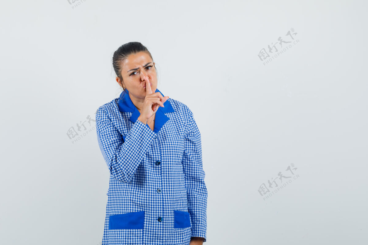睡衣一个年轻的女人 穿着蓝色方格布睡衣 摆出沉默的姿势 把食指放在嘴唇上 表情严肃 正面照年轻女孩沉默