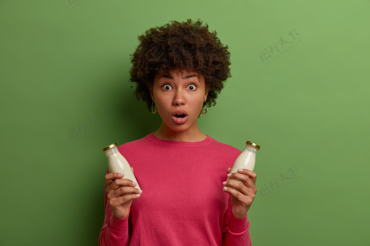 杏仁震惊的少数民族年轻女子喝有机杏仁或椰子奶 摆出健康的素食产品 非日记替代品 保持嘴巴张开 有适当的营养素食 吃牛奶套头衫奶瓶