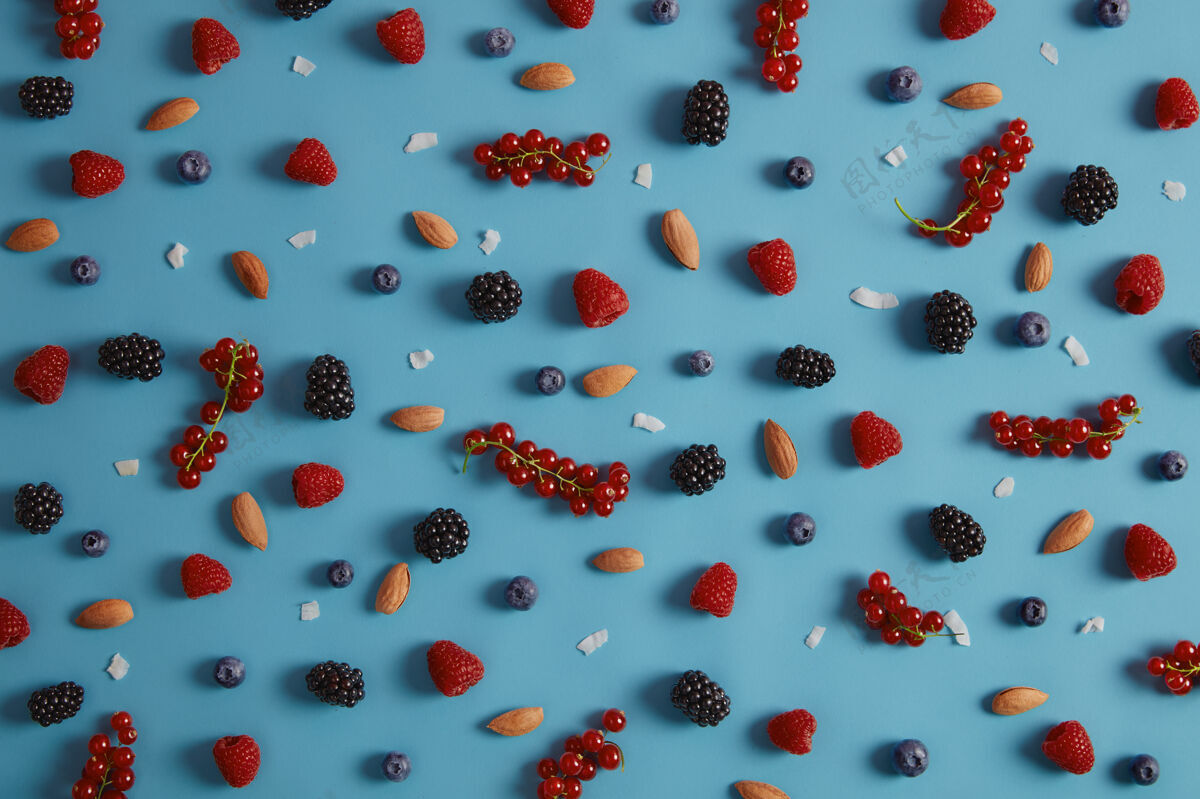 覆盆子混合各种新鲜浆果 包括覆盆子 蓝莓 黑莓 蓝背景红醋栗 杏仁和椰子片制作美味甜点的健康原料品种繁多混合配料黑莓