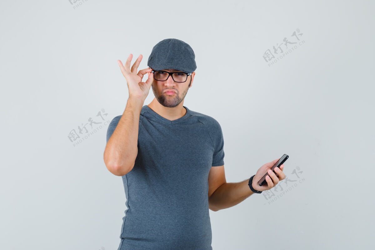 帽子一个戴着灰色t恤帽子拿着手机的年轻男人 看上去很可疑远观商务摄像头手机