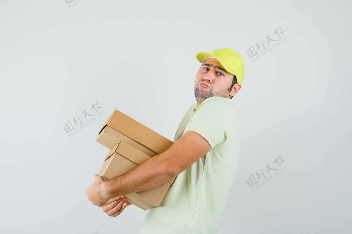 胡茬戴着t恤帽拿着沉重纸板箱的年轻人男衬衫硬纸板