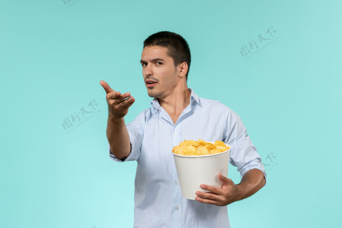 成人前视图年轻人拿着土豆cips在蓝色的墙上孤独的遥远的电影院电影乳制品土豆