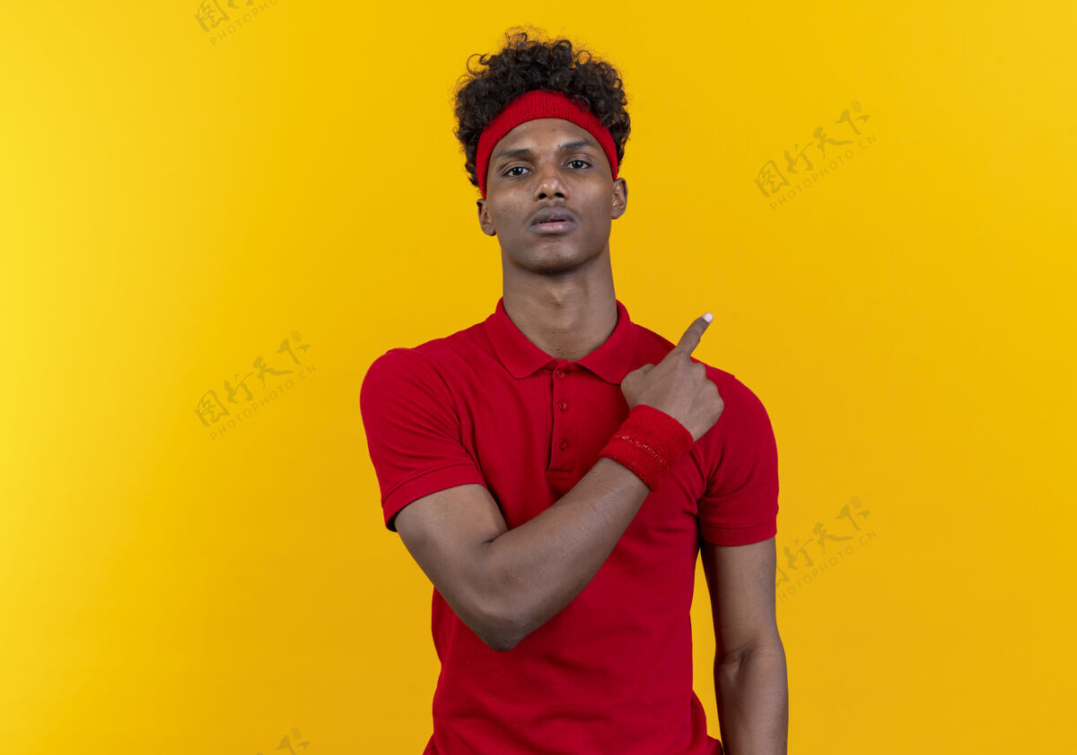 年轻看着镜头年轻的黑人运动男子戴着头带和腕带点在一边孤立的黄色背景与复制空间壁板穿头带