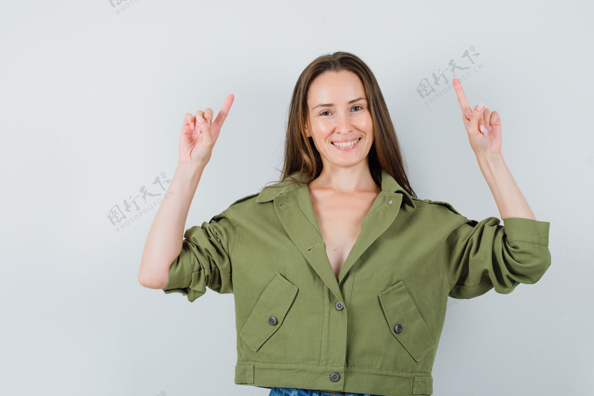 性感一位身穿绿色夹克的年轻女士指着头 看上去很高兴优雅指向向上