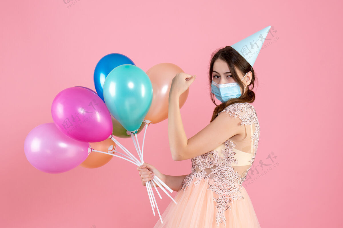 人正面图可爱的派对女孩 戴着派对帽 肌肉发达 手持五颜六色的气球站着举行站立庆祝