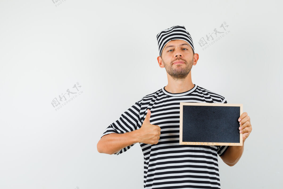 办公室年轻男子拿着黑板 戴着条纹t恤帽子 大拇指向上 看上去很自信专业家伙远景