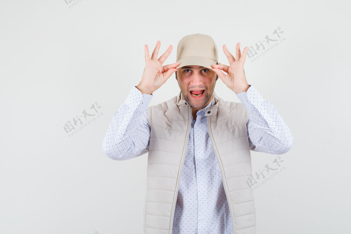 花花公子穿着米色夹克和帽子的年轻人把手放在帽子上 看起来很高兴 正前方的景色人男人脸