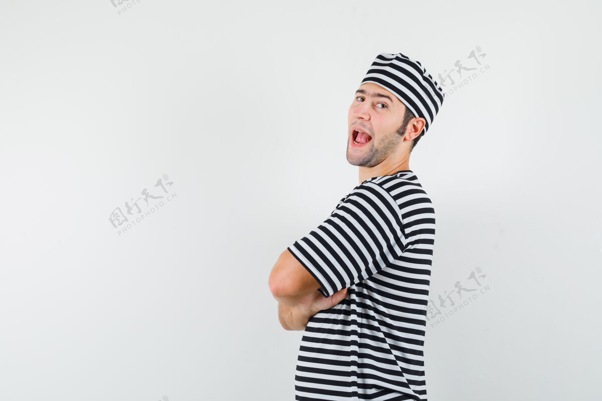 年轻年轻的男性交叉双臂站在t恤衫上 戴着帽子 看上去很自信花花公子人男性