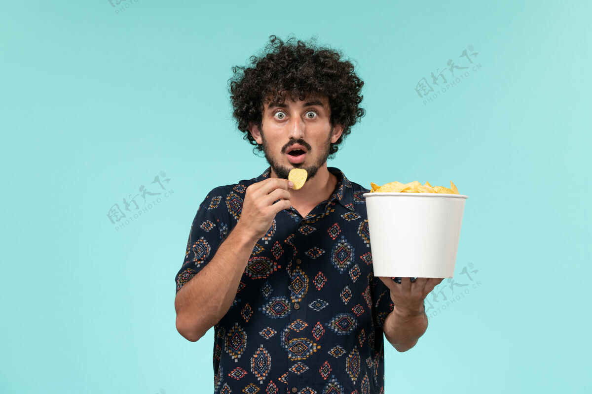 电影正面图年轻人拿着篮子和土豆cips在浅蓝色的墙上吃电影男杯子电影电影