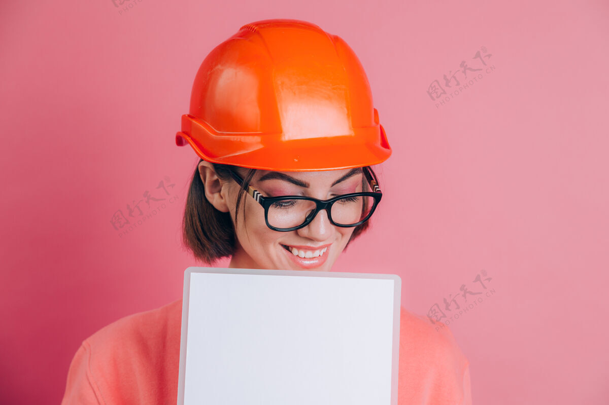 建筑面带微笑的女建筑工人手持白色的空白标志牌 背景是粉色的建筑头盔工作白承包商