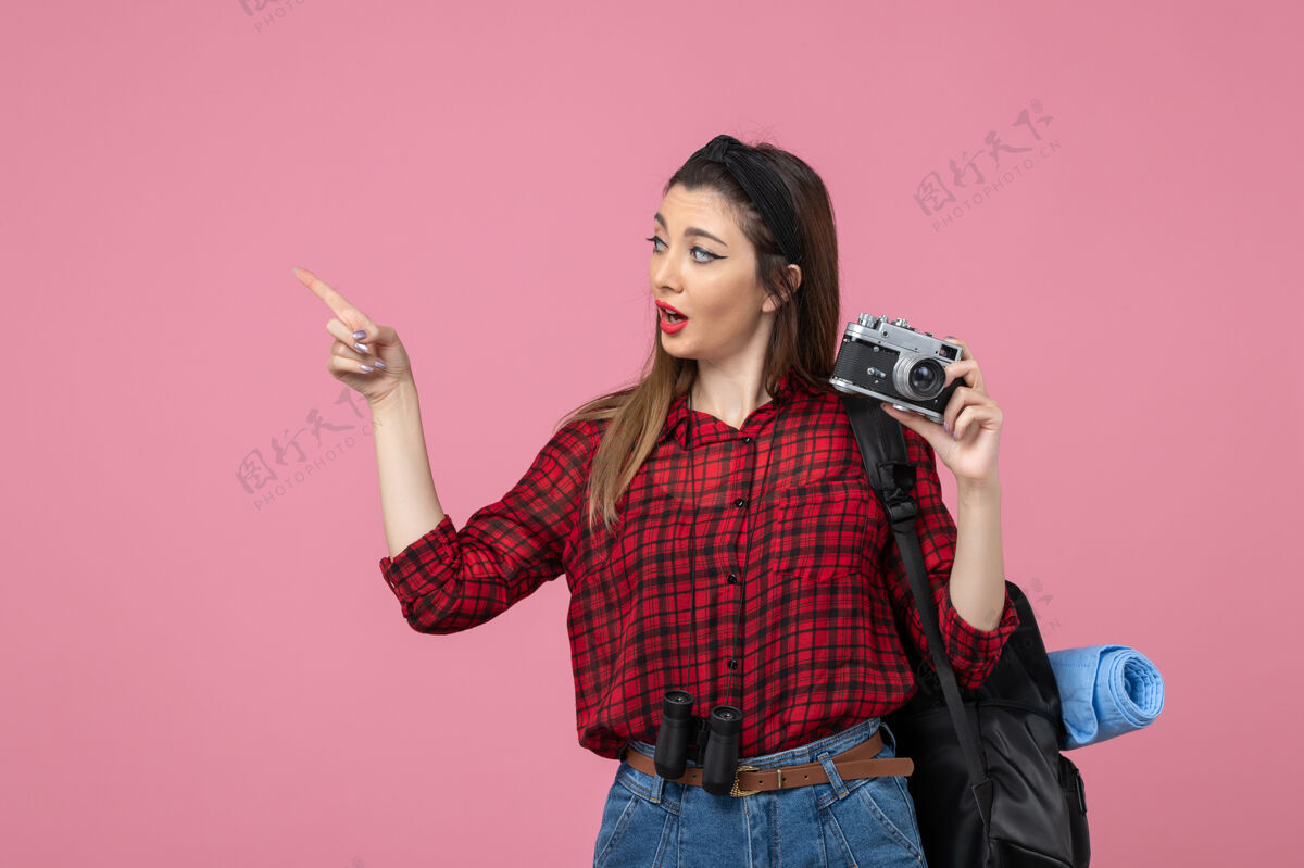微笑前视图年轻女性用相机在淡粉色背景上拍照女性照片模型照片人美丽