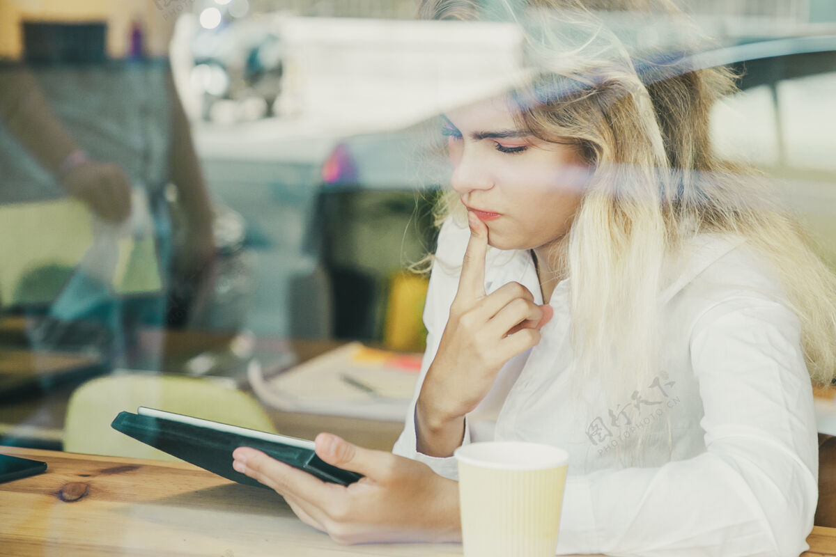 自由职业者沉思的女性专业人士坐在办公桌旁的共同工作空间或咖啡厅 使用平板电脑互联网项目女性