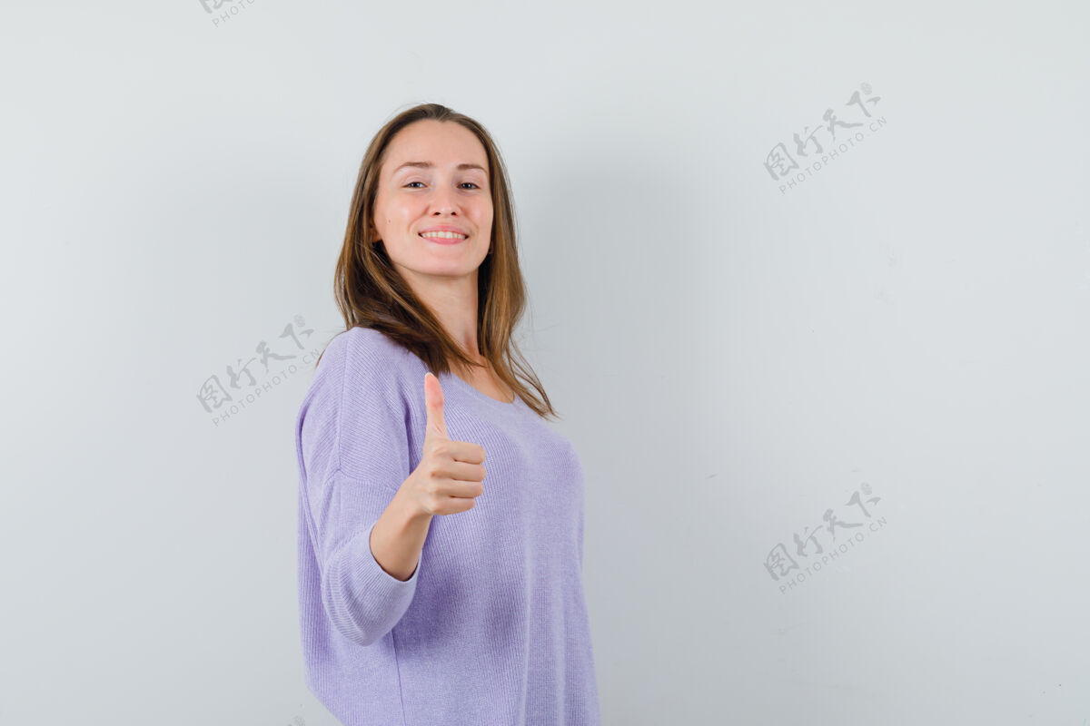 卷曲身穿淡紫色上衣的年轻女子竖起大拇指 看上去很高兴衬衫姿势自信
