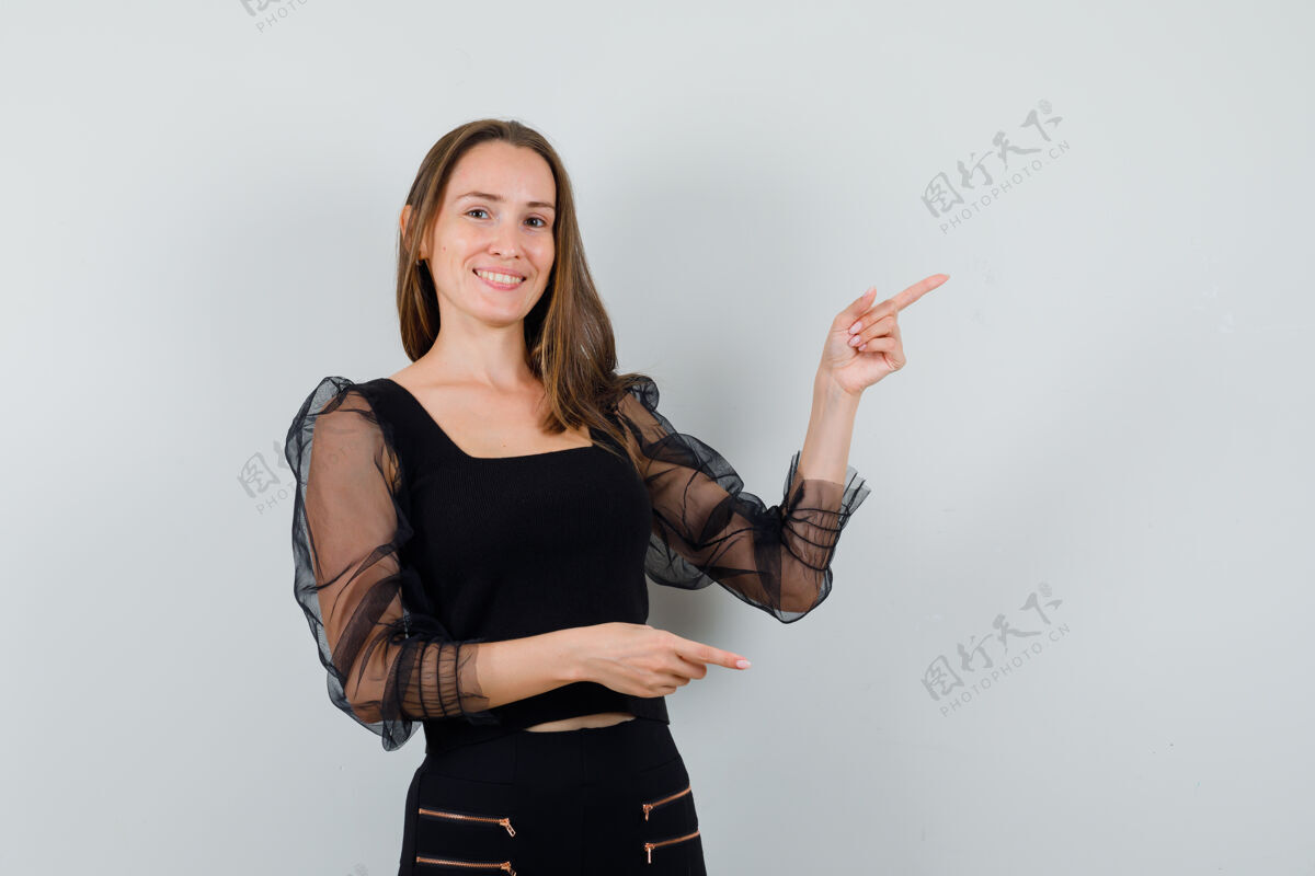 魅力一个年轻的女人用食指指着右边 穿着黑色上衣和黑色裤子 看上去很乐观女性黑发头发
