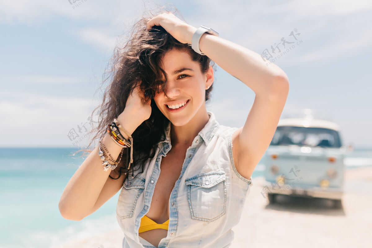放松阳光明媚的日子里 美丽的快乐女人 蓬松的卷发 在海边嬉皮货车旁摆姿势美丽时尚沙滩
