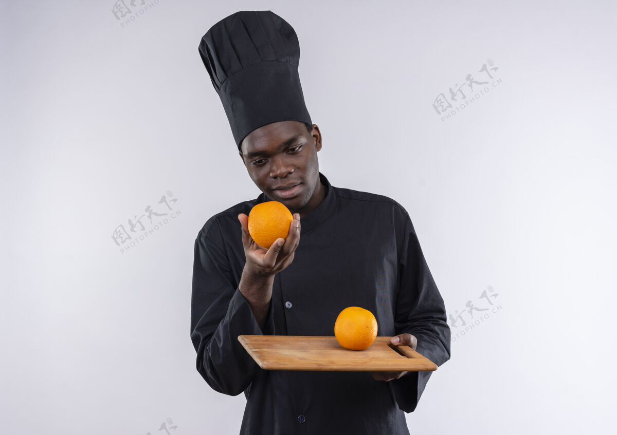 年轻年轻的美国黑人厨师身着厨师制服 手拿橘子放在砧板上 手拿白色 留有复印空间板空间橙色