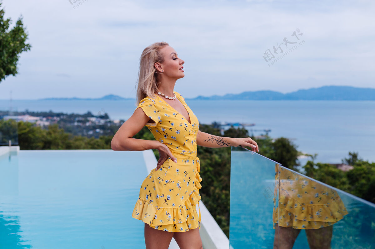 度假年轻的白种人平静快乐美丽的女人 带着明亮的晚妆 穿着夏天的黄色连衣裙和贝壳项链自由淑女时尚