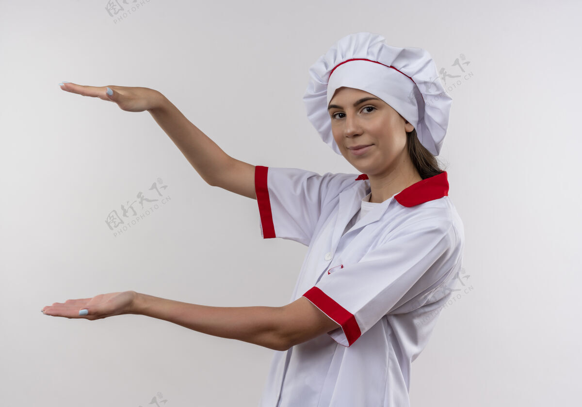 请穿着厨师制服的年轻快乐的白人厨师女孩站在一边 假装拿着白色的东西 留着复印空间侧年轻东西
