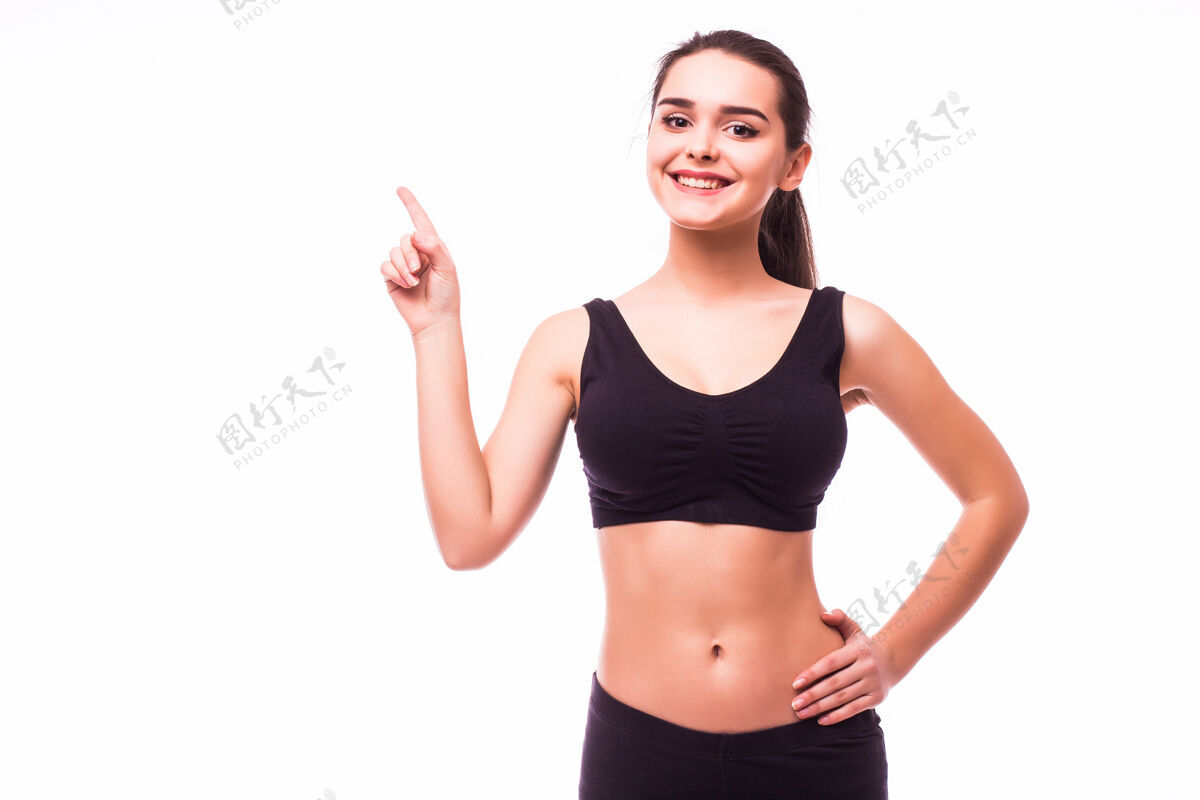 向上穿着运动服的快乐美丽的健身女士指着广告空间在白色背景上孤立指向健康站立