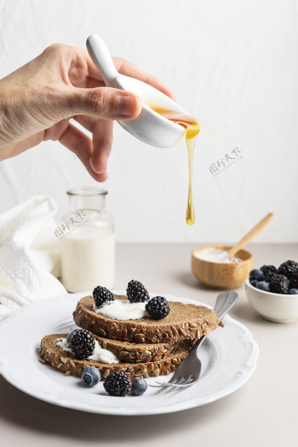 早餐用手把蜂蜜倒在烤面包和蓝莓上美味液体面包