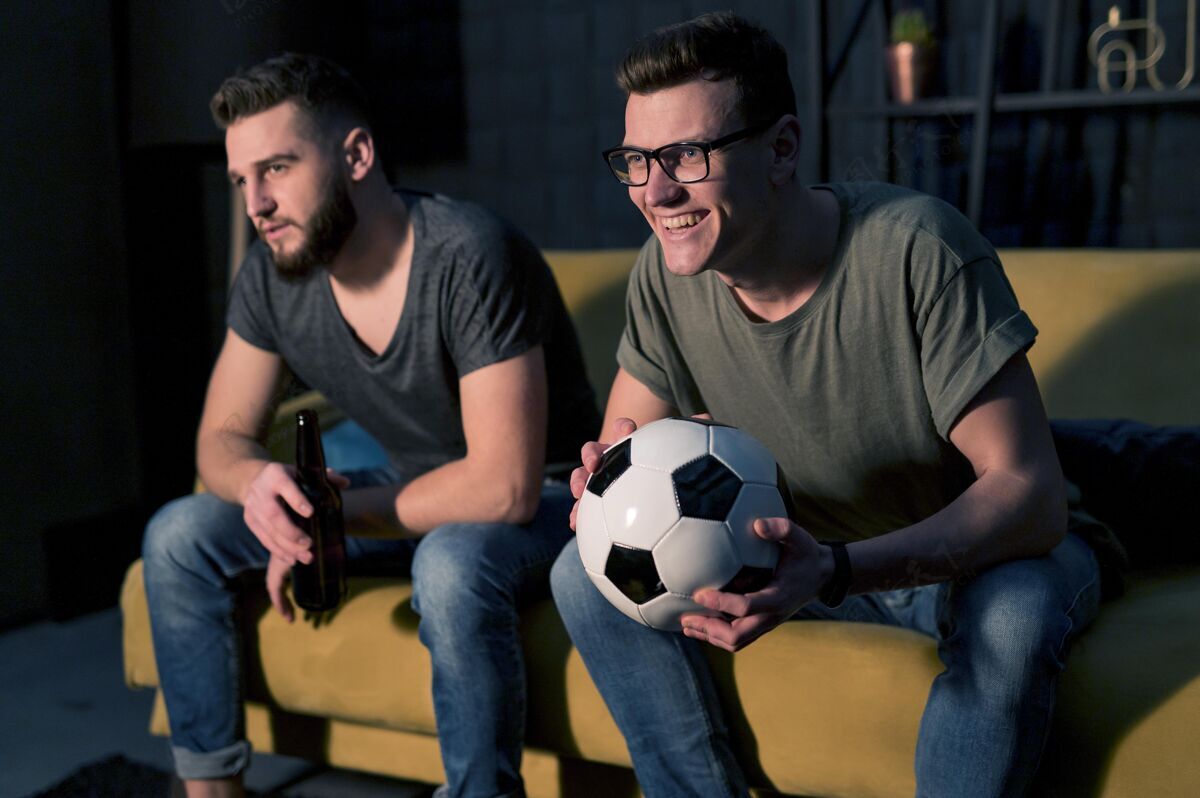 伙计笑眯眯的男朋友们一边看电视上的体育节目一边举行足球赛最好的朋友看电视最好的朋友