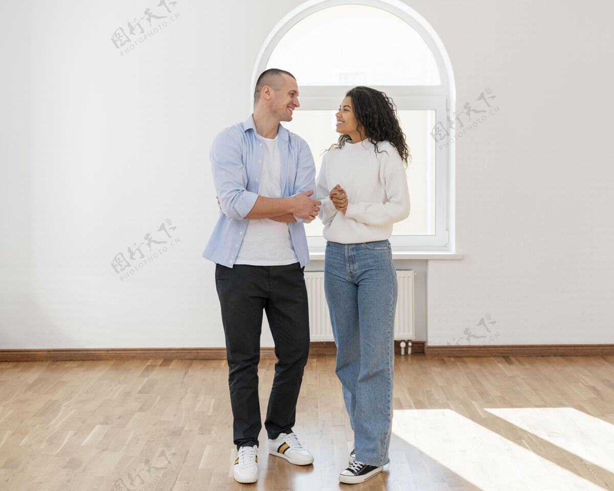 夫妻笑脸夫妇在他们新的空房子的正面视图职业住宅所有权