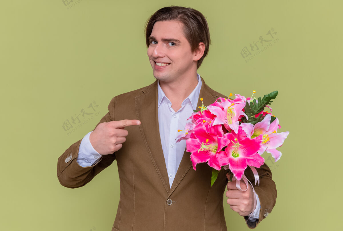 指着快乐的年轻人拿着花束 用食指指着花束 满脸笑容 站在绿色的墙壁上 向国际妇女节的理念表示祝贺女人花男人