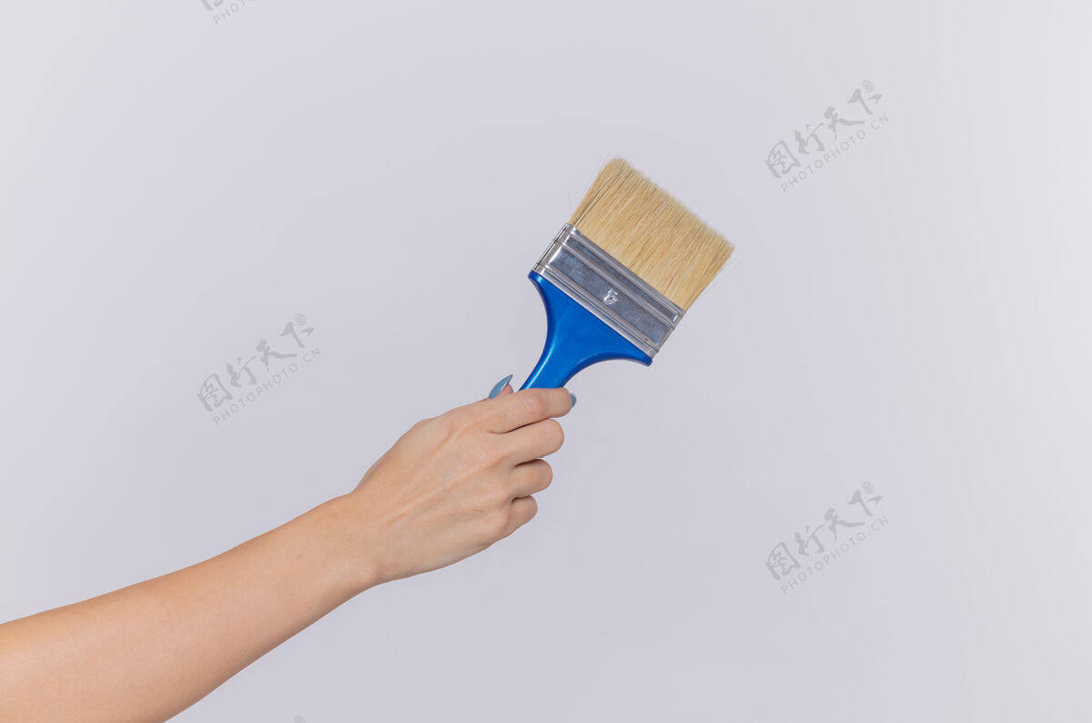 握着剪短照片的手拿着油漆刷的妇女在孤立的白色墙壁刷子女人手