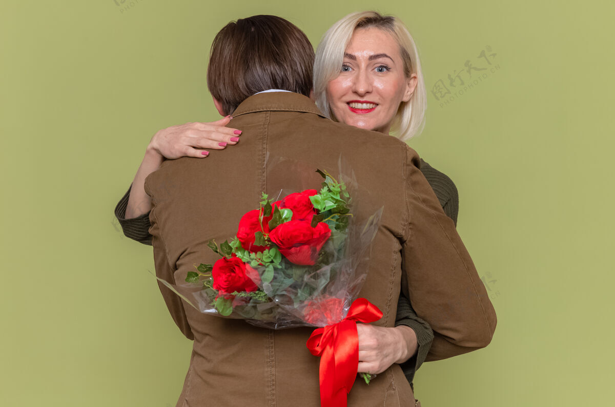 男人年轻美丽的情侣幸福的男人和女人用花束拥抱幸福的爱情一起微笑着庆祝国际妇女节站在绿色的墙上一起爱女人