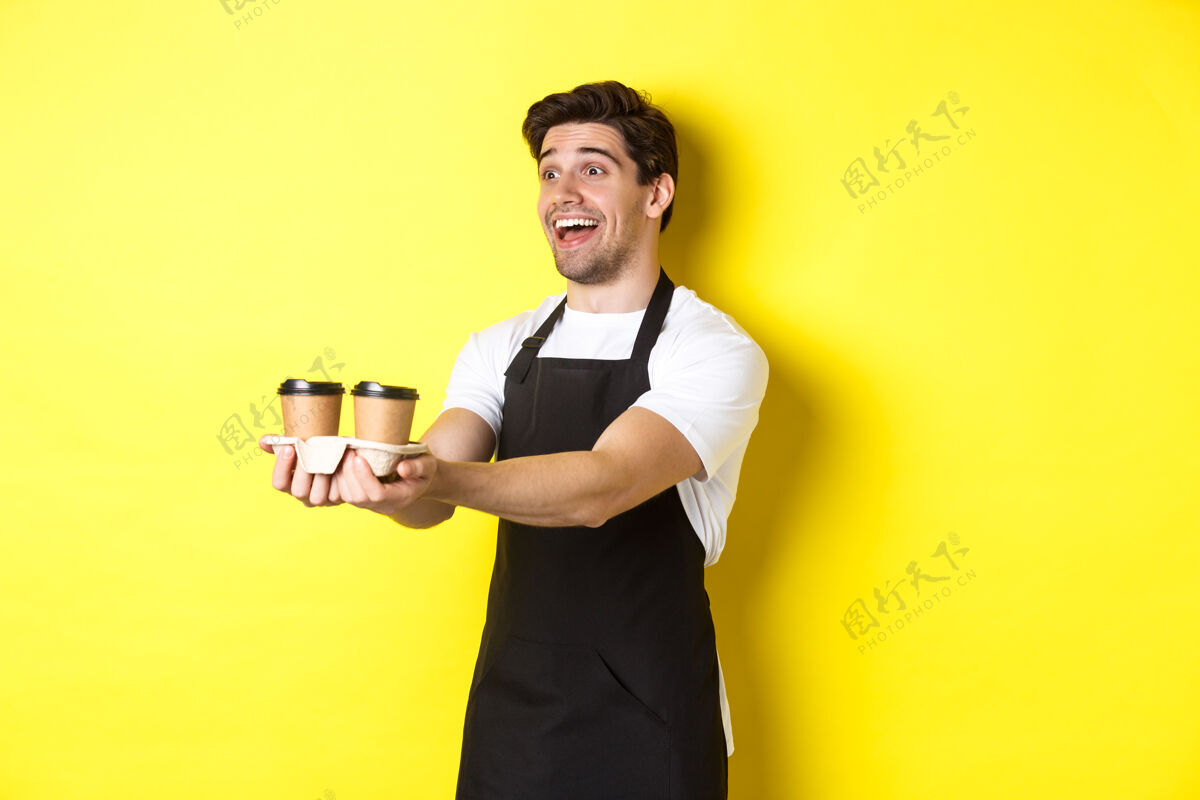 咖啡友好的咖啡师 穿着黑色围裙 端着两杯咖啡 微笑着 站在黄色的背景上表情黄色成人
