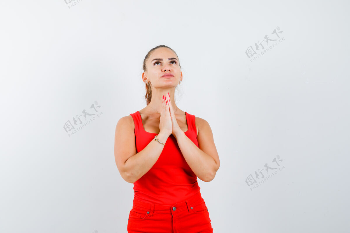 成人年轻的女士手牵手在祈祷的姿态在红色的单打 红色的裤子 并期待着希望 前方的看法女孩前面女人