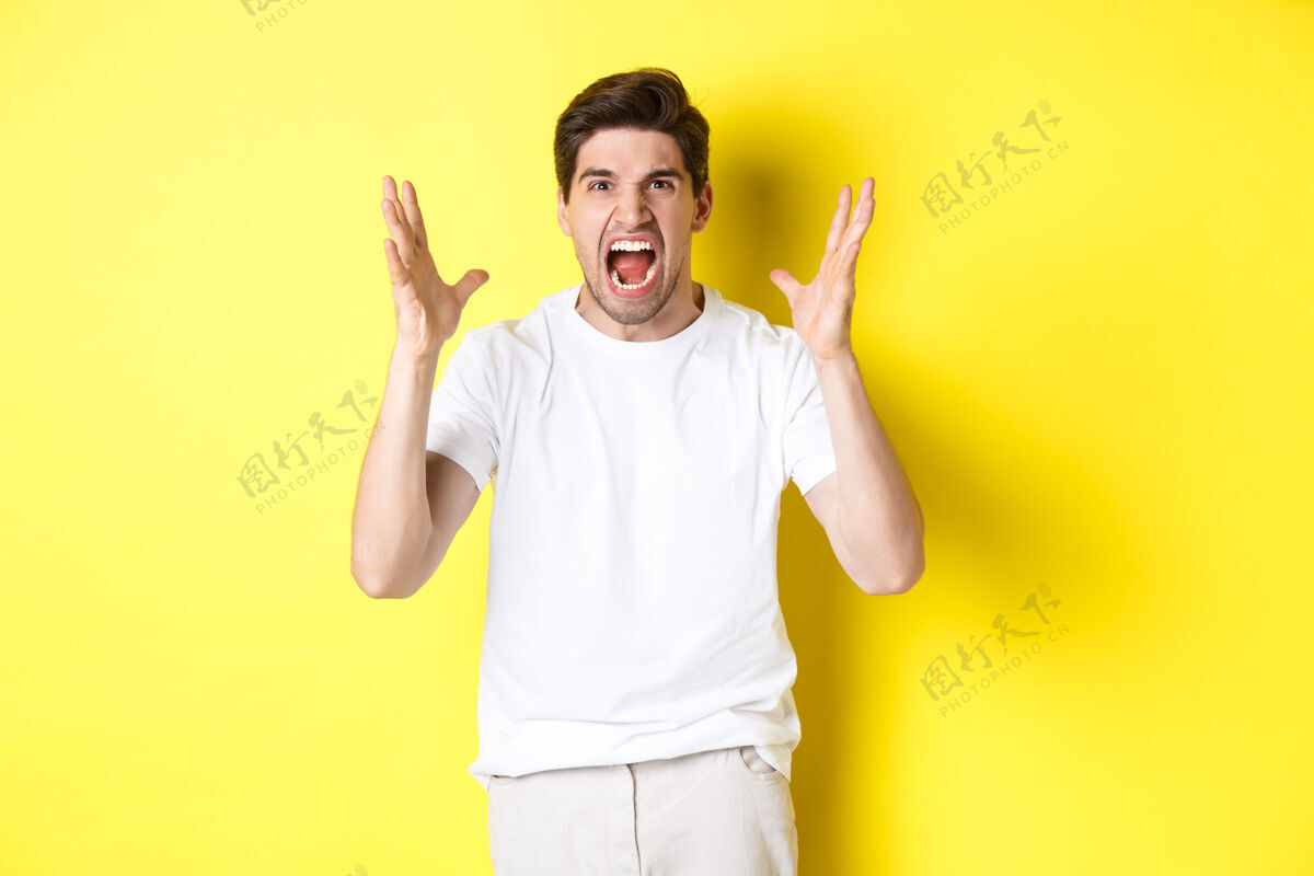 男人愤怒的男人大喊大叫 握手 带着仇恨做鬼脸 站在黄色背景下复制空间时尚黄色工作室