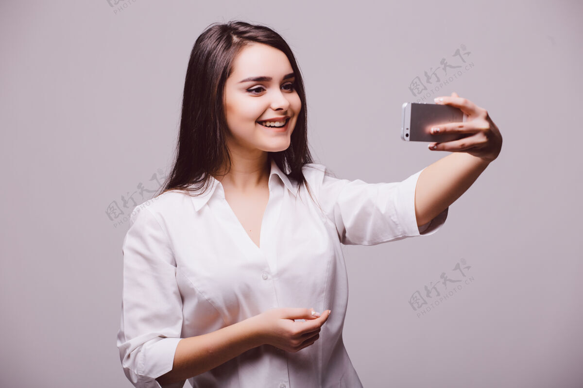 电话一位面带微笑的年轻迷人的女士 手拿数码相机 在白色背景下拍摄自拍女人微笑女孩