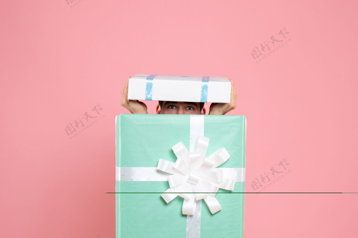 正面正面图年轻男性试图隐藏在礼物盒内的粉红色圣诞色情感睡衣派对游戏情绪试试派对