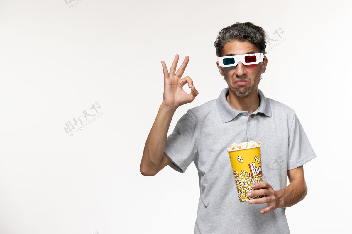 太阳镜正面图：戴着d型太阳镜的年轻男性手持爆米花 表面呈浅白色遥远前面电影院