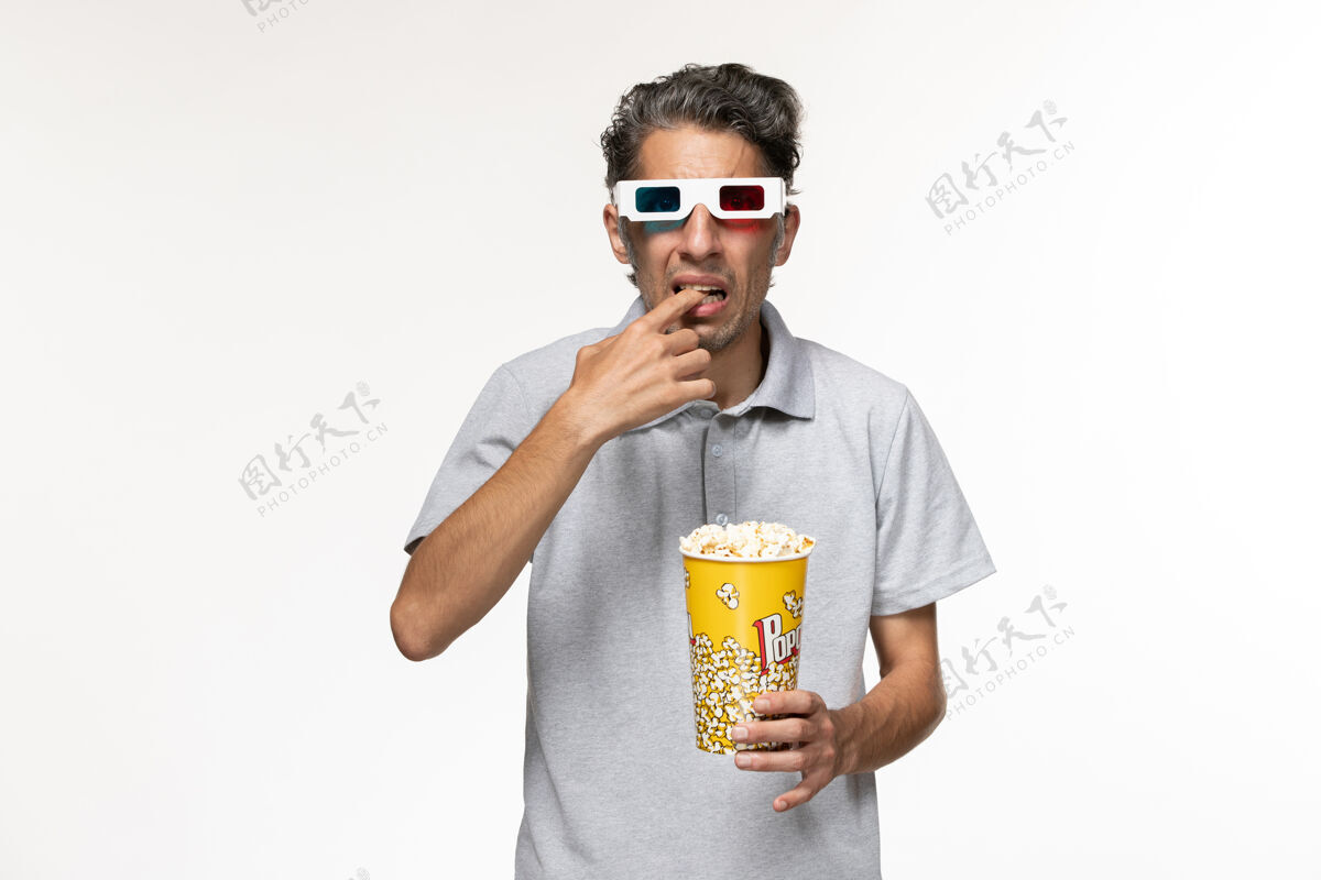 电影正面图：年轻男性戴着d型太阳镜坐在白色桌子上吃爆米花啤酒杯啤酒电影院