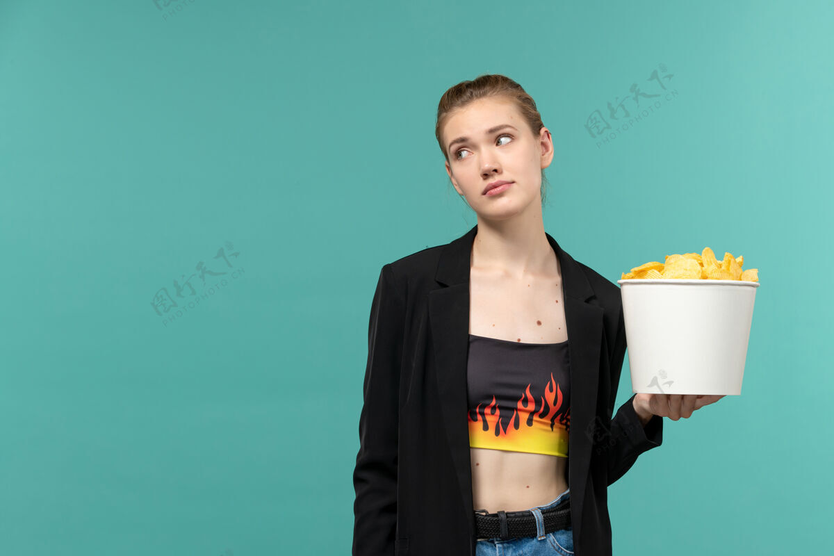 抱着正面图：年轻女性手持薯片 在浅蓝色的表面上看电影电影院土豆浅蓝色