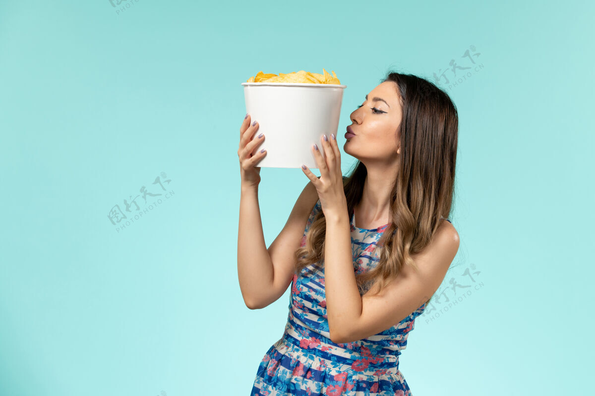 年轻女性正面图：年轻女性拿着一个装着薯片的包裹 在蓝色的表面亲吻它电影抱电影