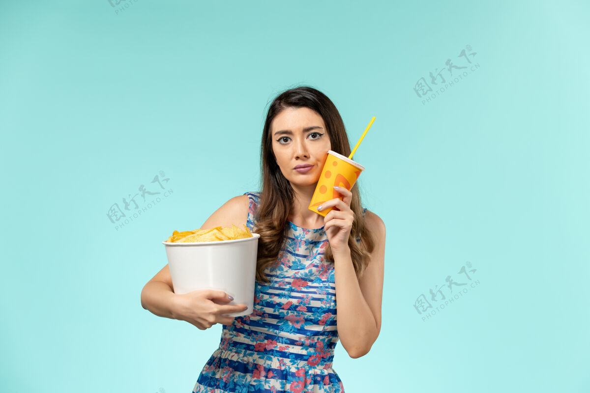 薯片正面图年轻的女性拿着篮子和薯片 在蓝色的表面上喝酒电影电影院杯子