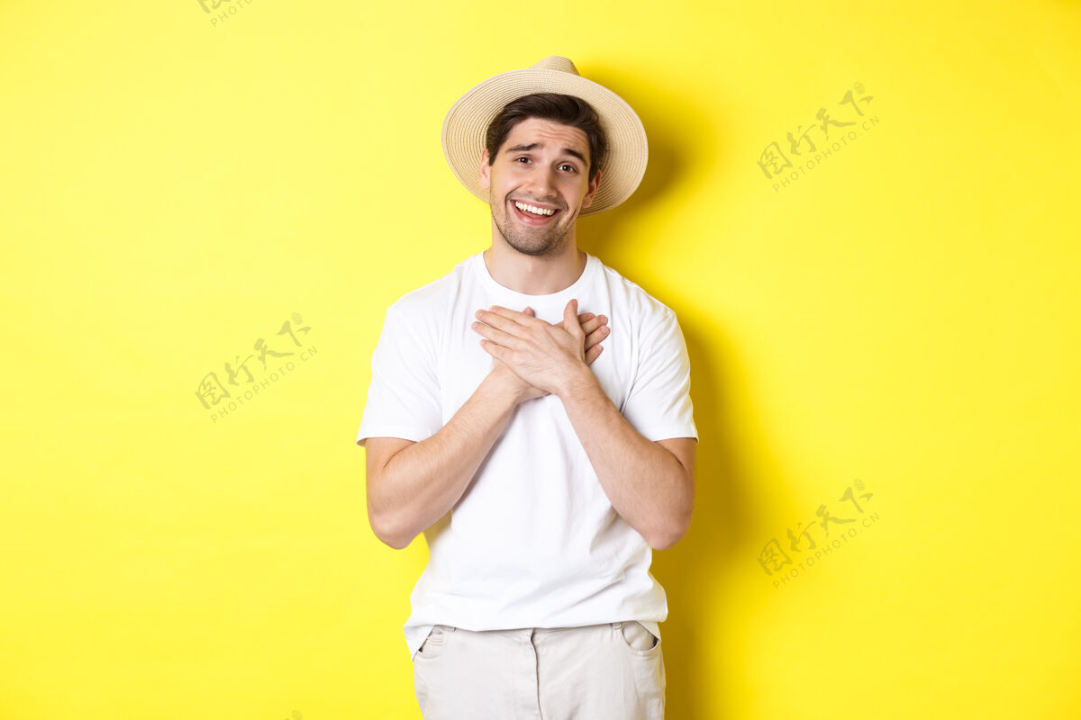 帽子旅游和避暑的概念带着草帽的感激的家伙手牵手在心上 说谢谢 微笑着感激 站在黄色的背景下黄色年轻表情