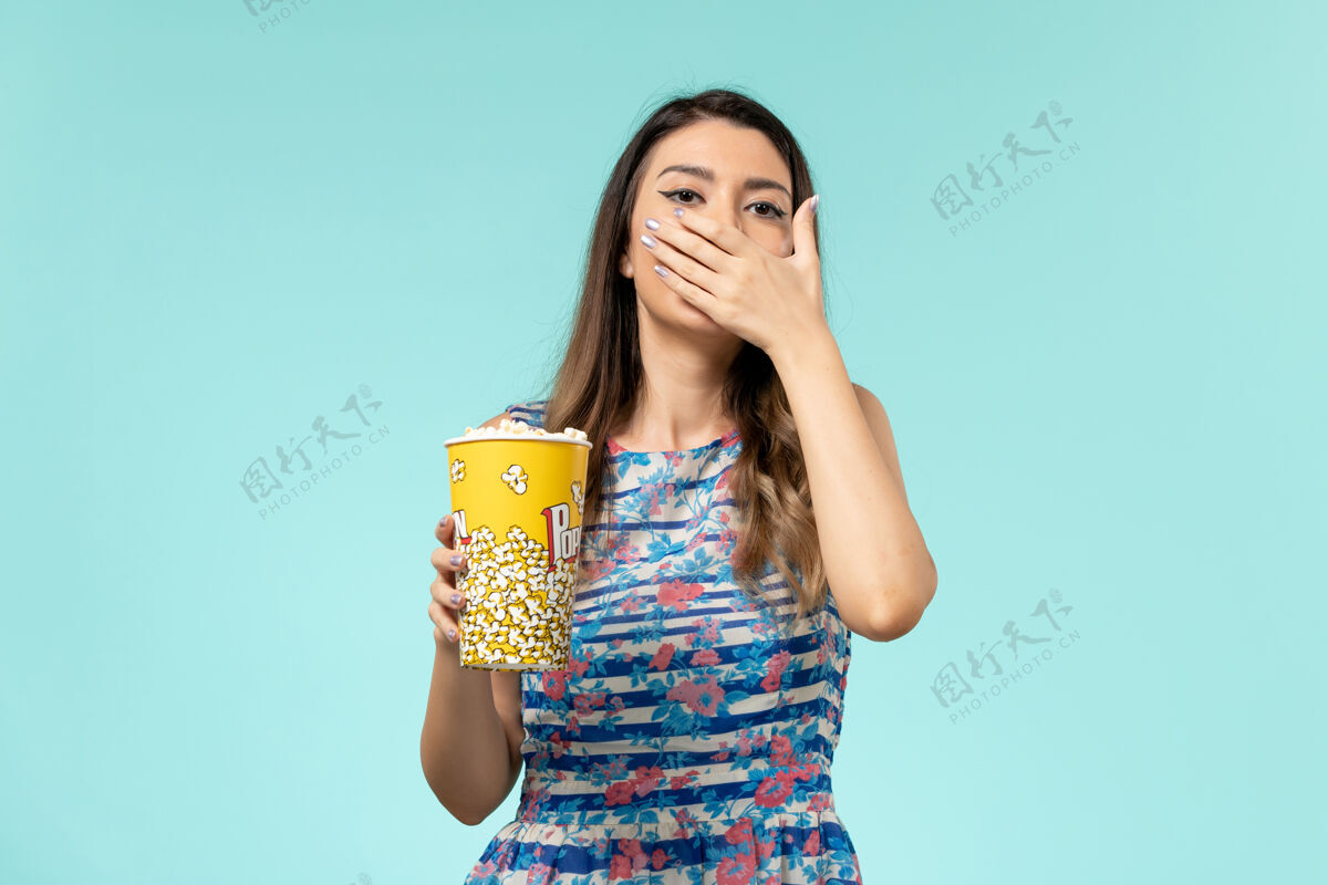电影院正面图：年轻女性手持爆米花包 在蓝色表面看电影看性感漂亮