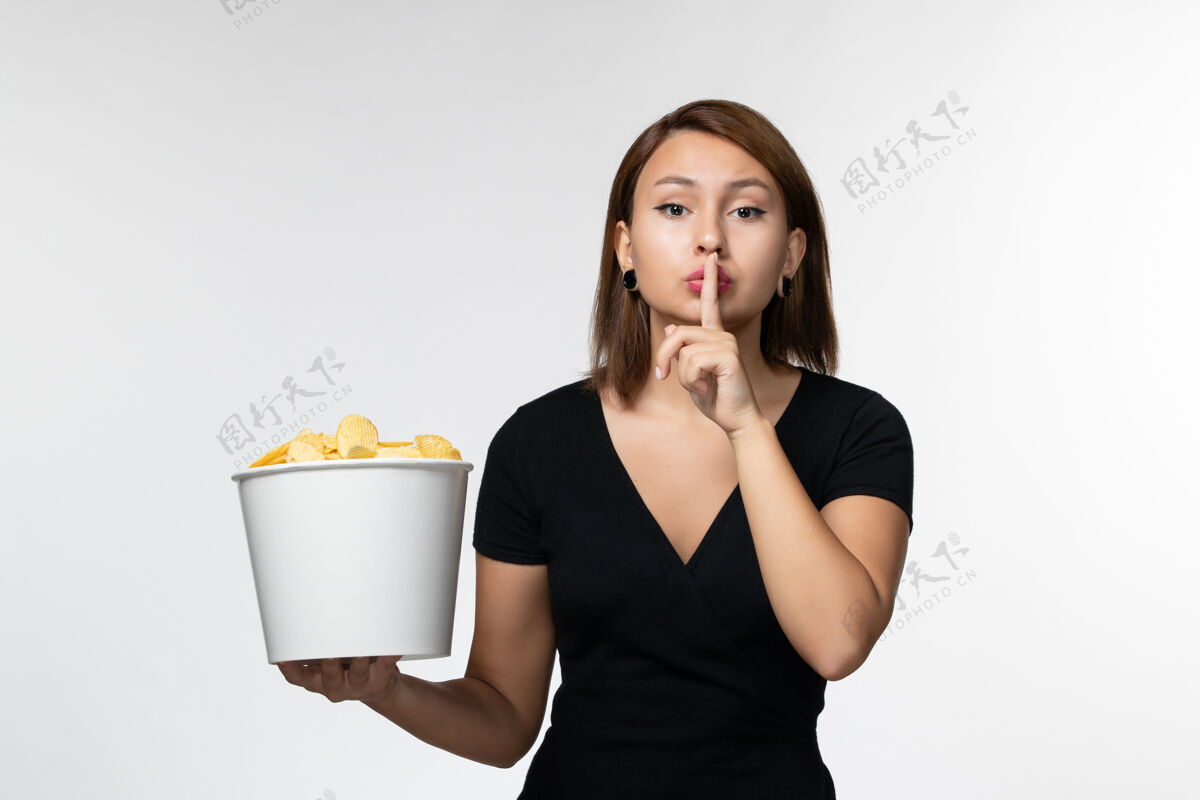 孤独正面图：年轻的女性拿着土豆片的篮子 在白色的桌子上摆姿势抱着前面书桌