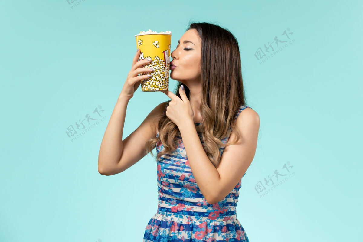 亲吻正面图年轻的女性拿着爆米花包在蓝色的表面亲吻它电影院包装剧院